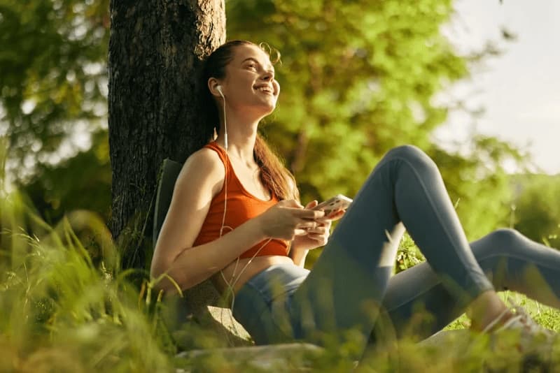 Imagem de uma jovem sentada em um parque ouvindo música com fones de ouvido