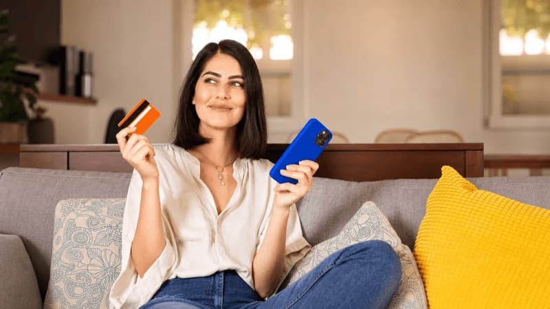 Imagem de mulher com celular e cartão do banco